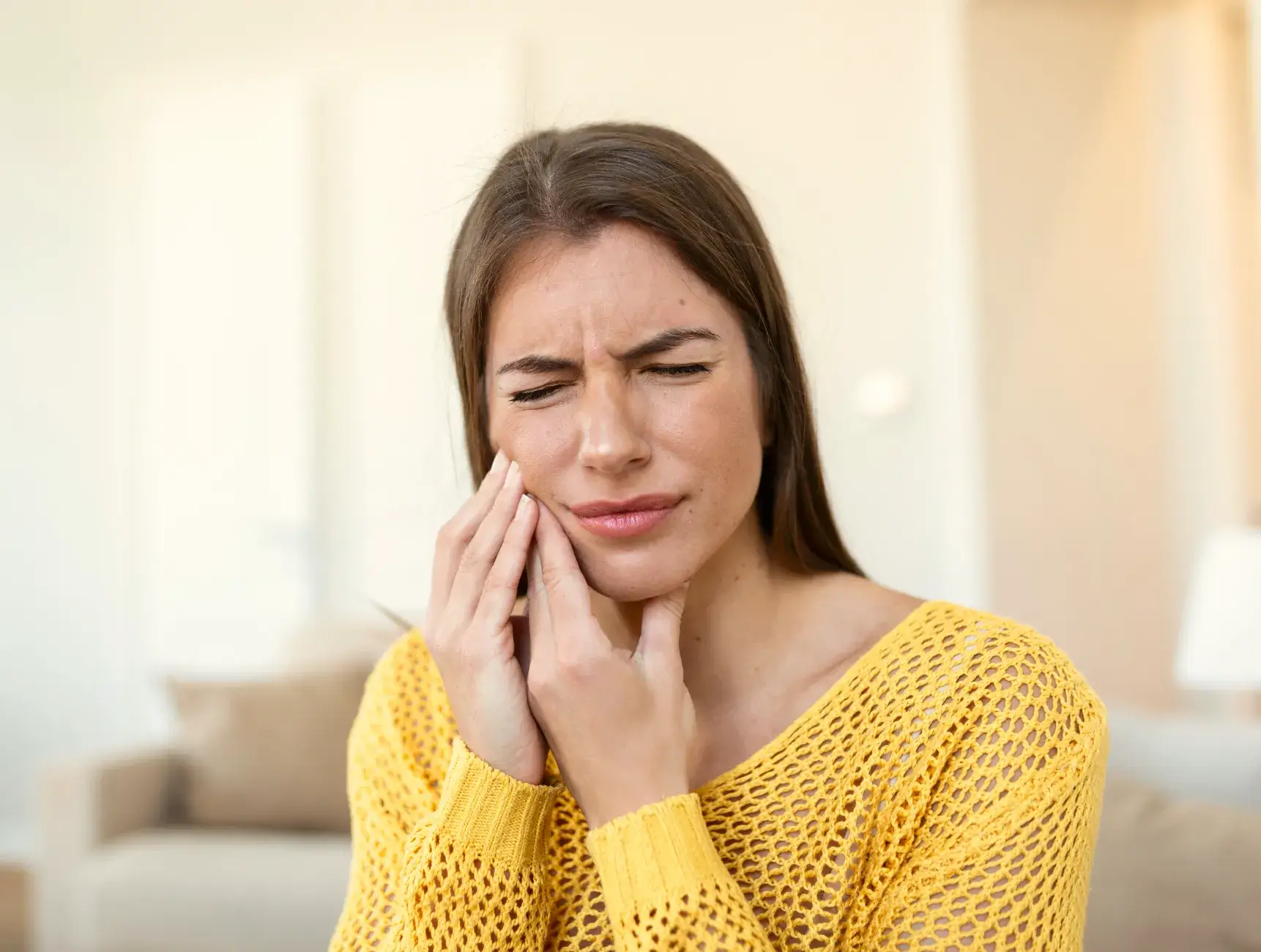 A woman in a yellow sweater holding her hand to her face.
