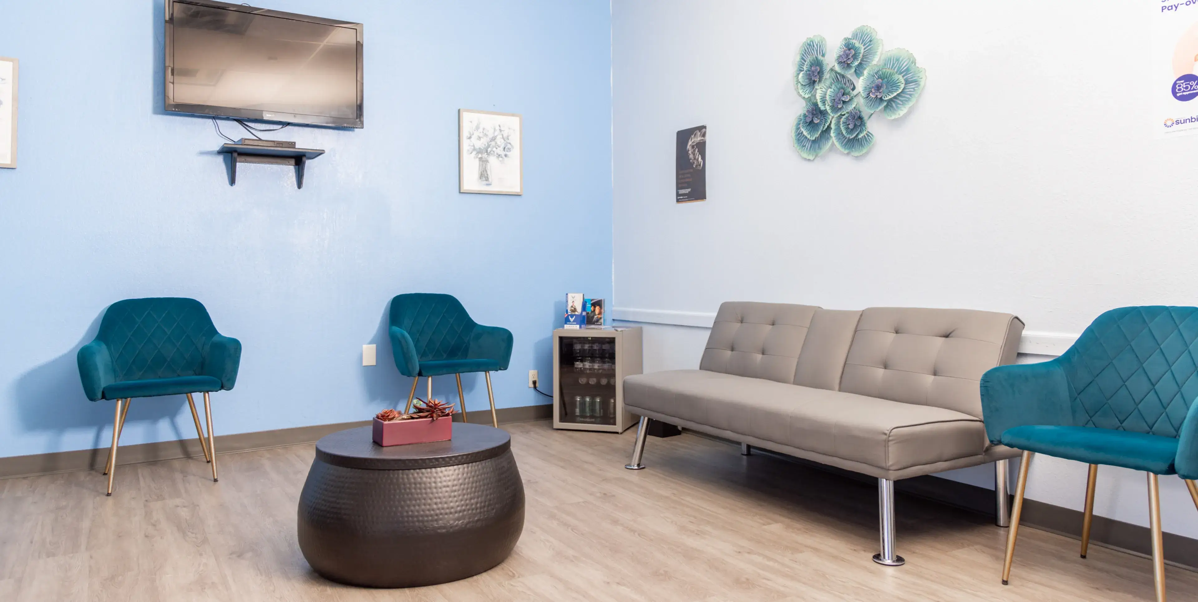 A waiting room with blue chairs and a flat screen tv.